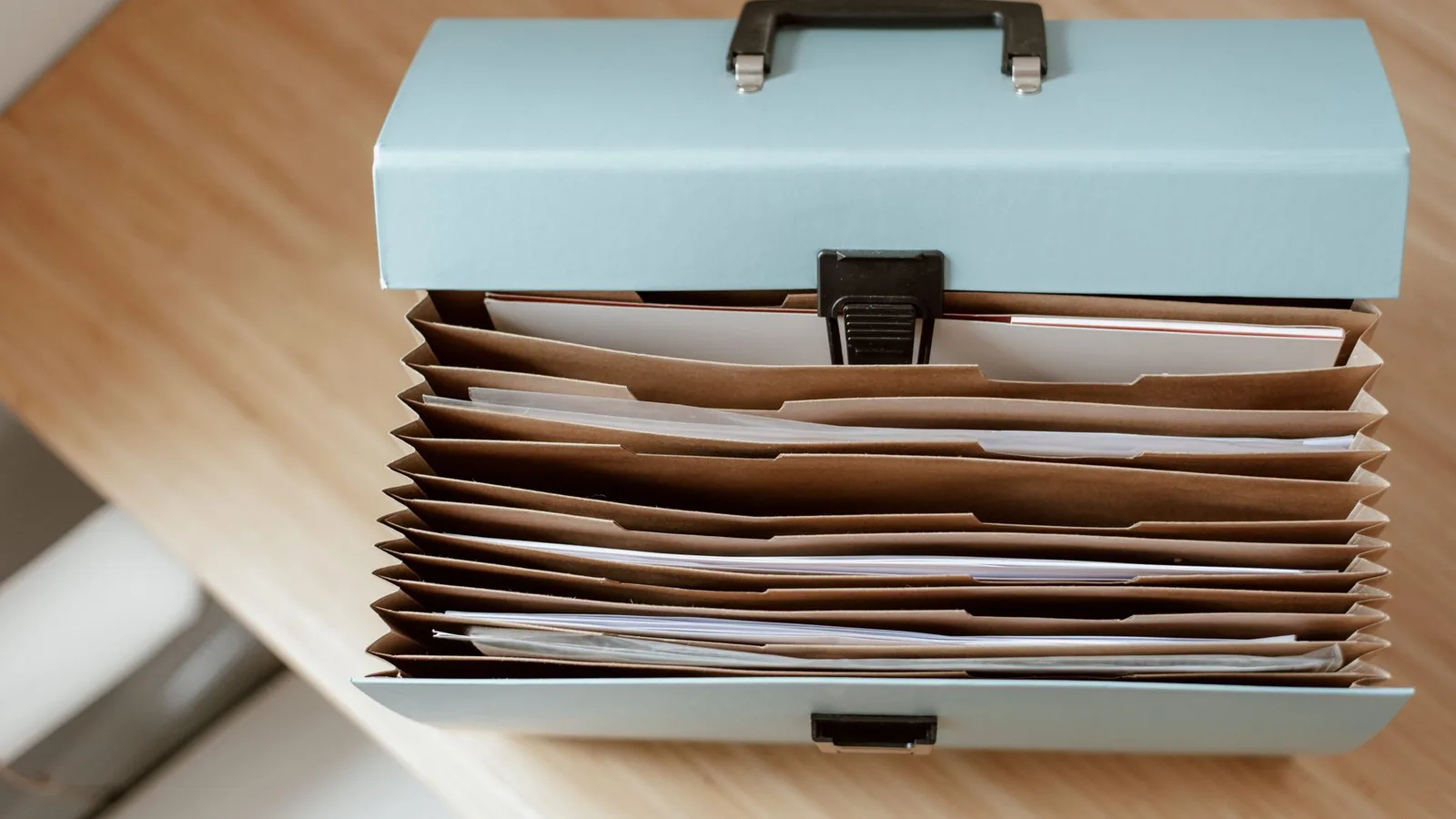 A file box of documents with papers on a wooden table in daylight.